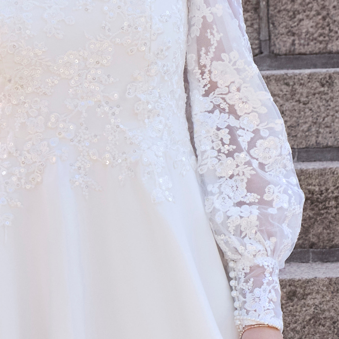 pige i konfirmationskjole med lange, voluminøse blondeærmer med glitter og perleknapper på manchetten