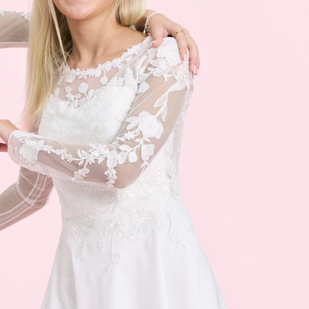 pige viser langt ærme og overdel på hvid konfirmationskjole i glitterblonde