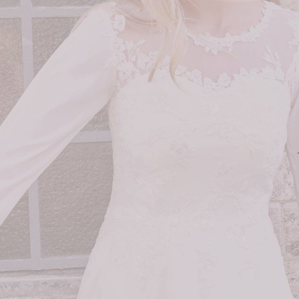 Pige viser konfirmationskjole med blonde, der fader lidt nedover underdelen i chiffon og ud på skuldrene. 