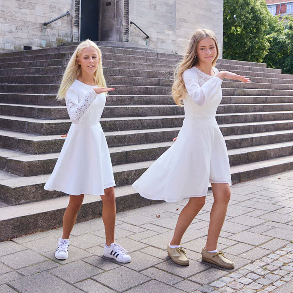 to piger danser i hvide konfirmationskjoler med lange ærmer foran kirke 